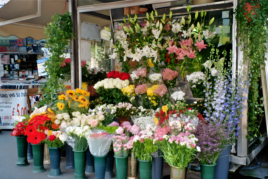 A vibrant floral display outside a flower shop features an assortment of fresh flowers arranged in bouquets and vases, including white lilies with large, trumpet-shaped petals and prominent stamens, p